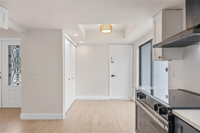 kitchen featuring electric range, wall chimney range hood, a tray ceiling, and light hardwood / wood-style flooring