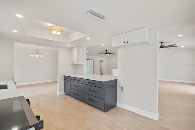 kitchen with a raised ceiling, white cabinetry, light wood-type flooring, gray cabinetry, and ceiling fan with notable chandelier