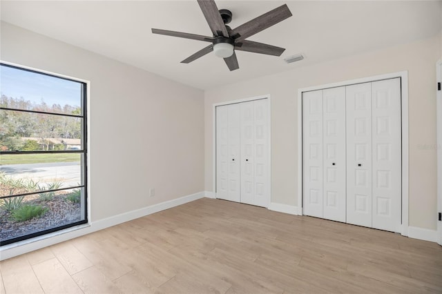 unfurnished bedroom with multiple closets, light hardwood / wood-style floors, and ceiling fan