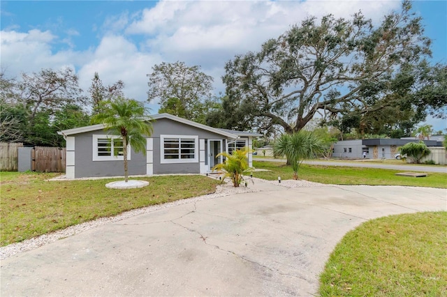 view of front of house featuring stucco siding, concrete driveway, a front lawn, and fence