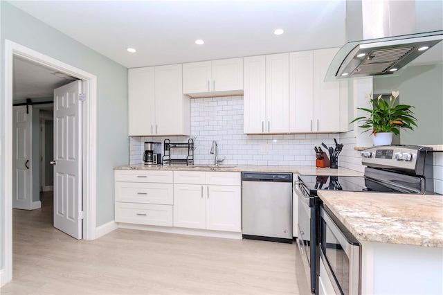 kitchen featuring a barn door, appliances with stainless steel finishes, light wood-type flooring, white cabinets, and wall chimney range hood