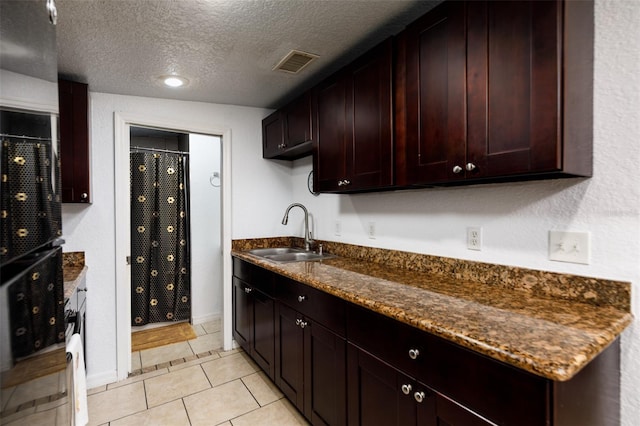 kitchen featuring a textured ceiling, sink, light tile patterned floors, dark stone counters, and dark brown cabinetry