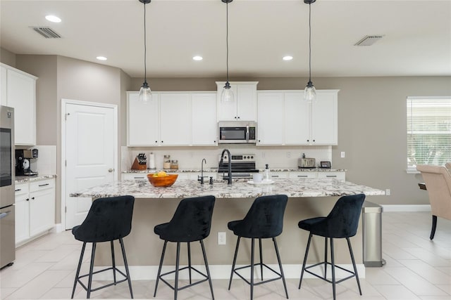 kitchen featuring a center island with sink, stainless steel appliances, tasteful backsplash, hanging light fixtures, and sink