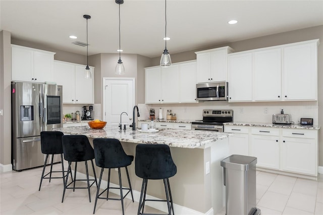 kitchen with white cabinetry, stainless steel appliances, a center island with sink, and light stone counters