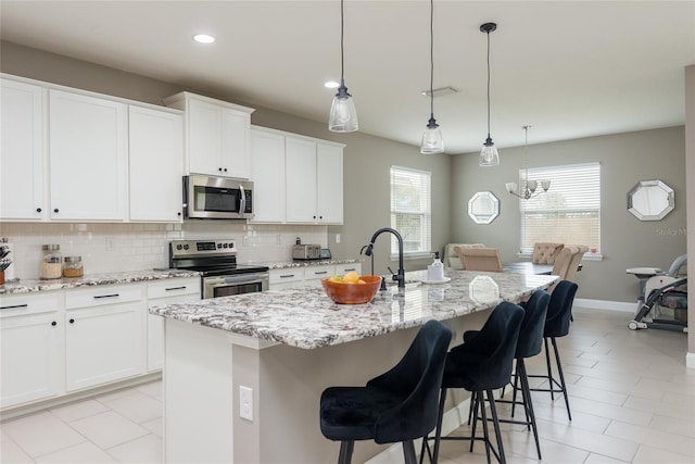 kitchen featuring decorative backsplash, white cabinetry, appliances with stainless steel finishes, and a kitchen island with sink