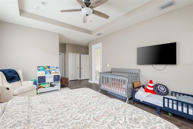 bedroom featuring dark hardwood / wood-style floors, ceiling fan, and a raised ceiling