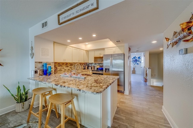 kitchen featuring stainless steel appliances, sink, white cabinets, light hardwood / wood-style flooring, and kitchen peninsula