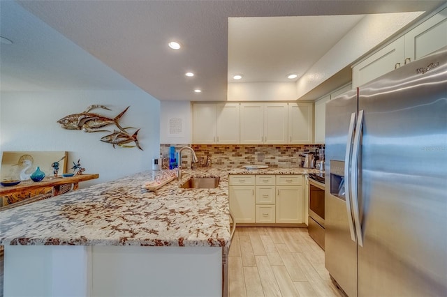 kitchen featuring appliances with stainless steel finishes, kitchen peninsula, decorative backsplash, sink, and light hardwood / wood-style flooring