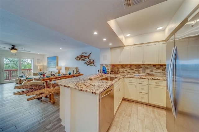 kitchen with sink, light wood-type flooring, kitchen peninsula, and appliances with stainless steel finishes