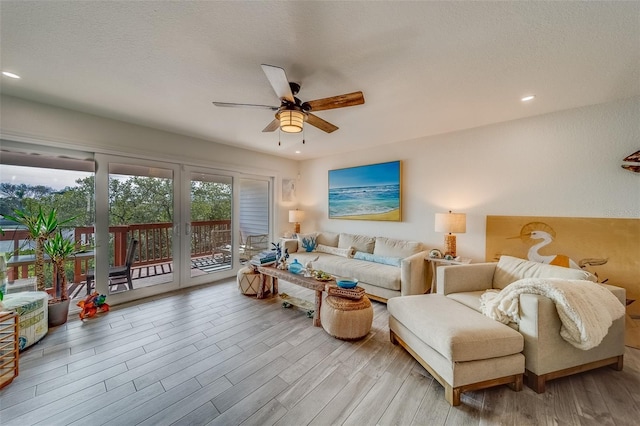 living room with ceiling fan, light wood-type flooring, and a textured ceiling