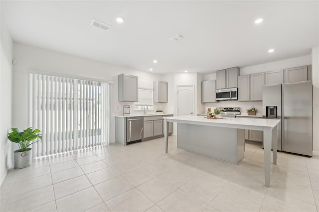 kitchen with gray cabinets, stainless steel appliances, a center island, a kitchen bar, and sink