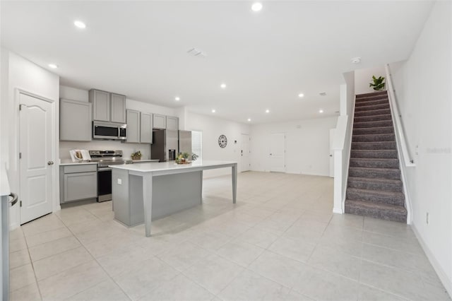 kitchen featuring an island with sink, light tile patterned floors, appliances with stainless steel finishes, and gray cabinets