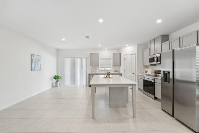 kitchen featuring stainless steel appliances, light tile patterned flooring, a breakfast bar area, a kitchen island, and gray cabinetry