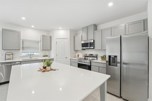 kitchen with sink, light tile patterned floors, a kitchen island, gray cabinetry, and appliances with stainless steel finishes