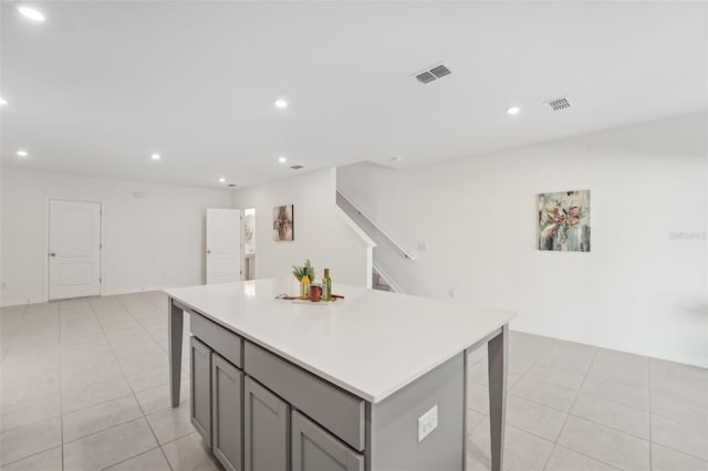 kitchen featuring a kitchen island, light tile patterned floors, gray cabinetry, and a kitchen bar