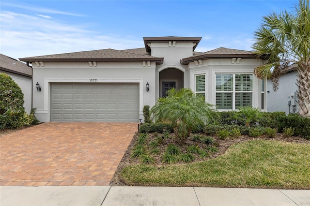 view of front of property with decorative driveway, an attached garage, and stucco siding