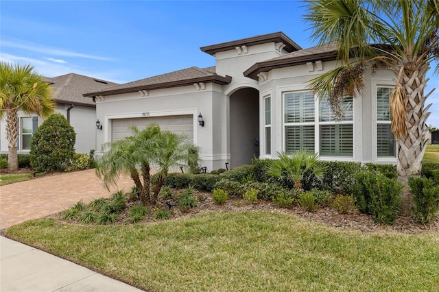 view of front of property with a front yard, decorative driveway, an attached garage, and stucco siding