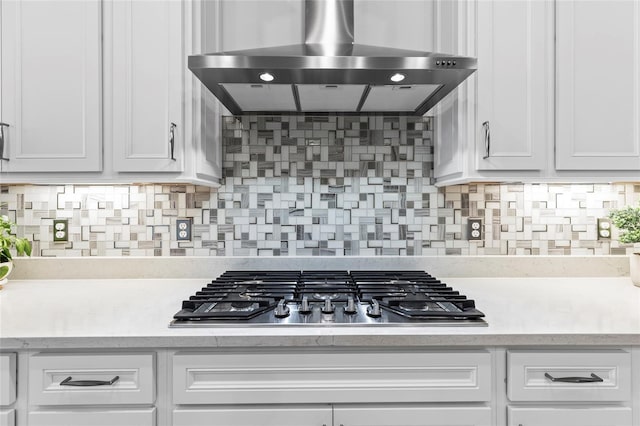 kitchen with tasteful backsplash, wall chimney range hood, white cabinets, and stainless steel gas stovetop