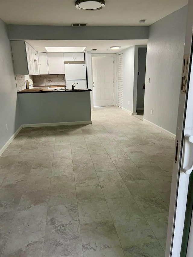 kitchen featuring tasteful backsplash, white fridge, white cabinetry, and kitchen peninsula