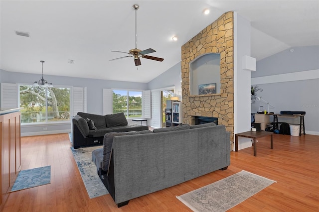 living room with ceiling fan with notable chandelier, vaulted ceiling, hardwood / wood-style flooring, and a stone fireplace