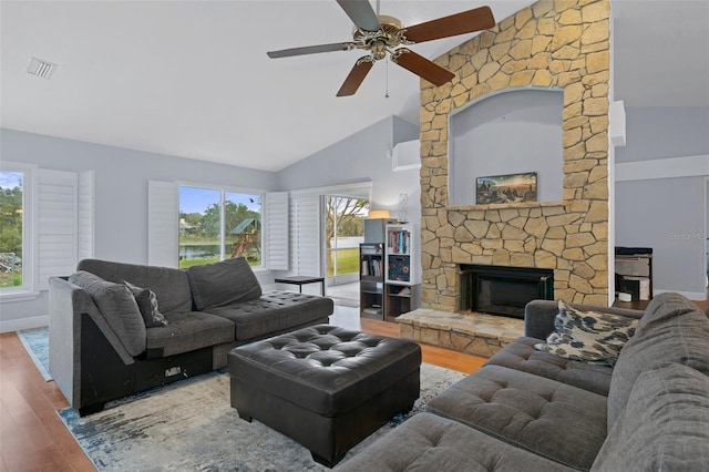 living room featuring high vaulted ceiling, ceiling fan, wood-type flooring, and a stone fireplace