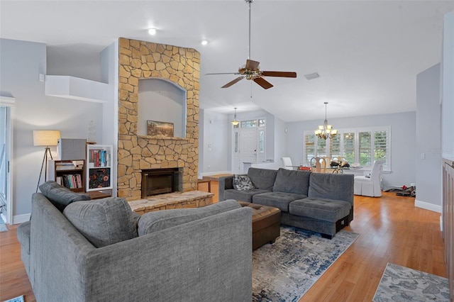 living room featuring ceiling fan with notable chandelier, high vaulted ceiling, light wood-type flooring, and a stone fireplace