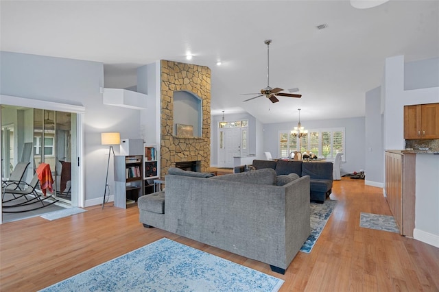 living room featuring light wood-type flooring, a stone fireplace, high vaulted ceiling, and ceiling fan with notable chandelier