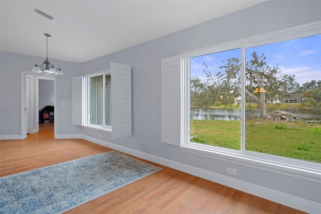 empty room with hardwood / wood-style floors, a chandelier, and a water view