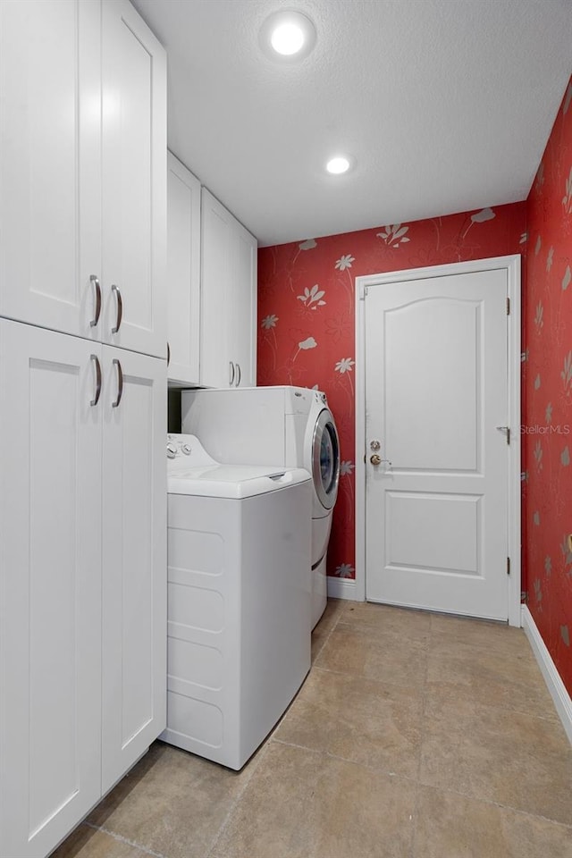 clothes washing area featuring a textured ceiling, cabinets, and washer and clothes dryer