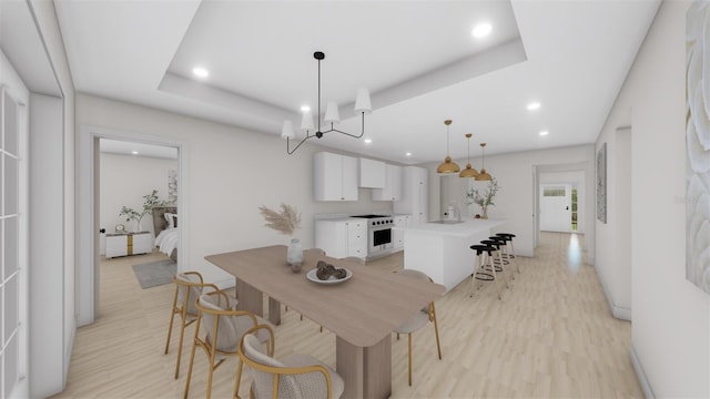 dining space featuring light hardwood / wood-style flooring, an inviting chandelier, and a raised ceiling