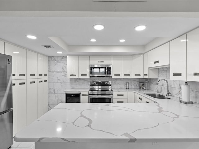 kitchen featuring light stone countertops, sink, stainless steel appliances, and white cabinetry