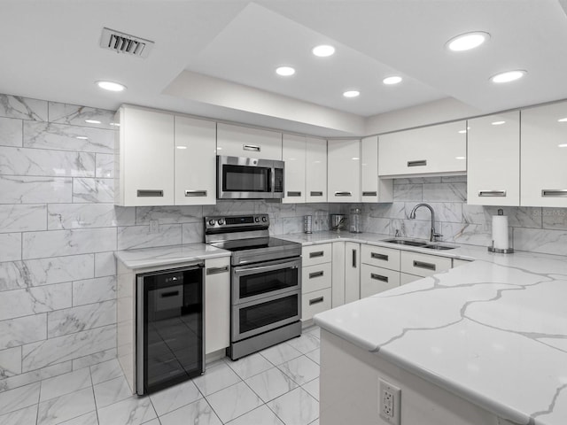 kitchen with light stone countertops, beverage cooler, white cabinetry, stainless steel appliances, and sink