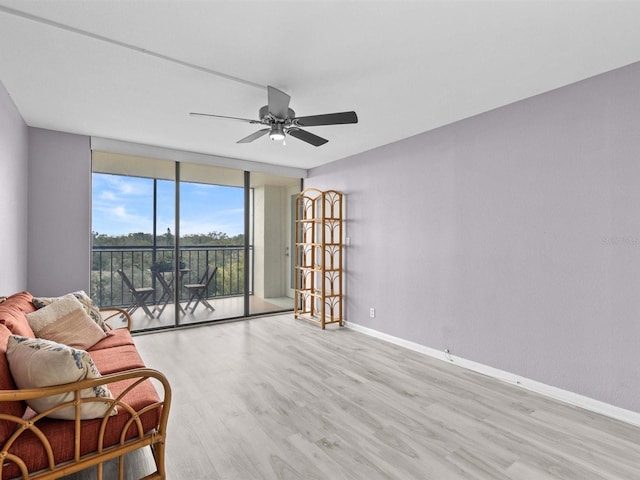 living area with ceiling fan, a wall of windows, and light hardwood / wood-style floors