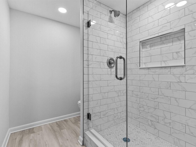 bathroom with toilet, a shower with shower door, and hardwood / wood-style flooring