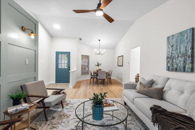 living room featuring ceiling fan with notable chandelier, light hardwood / wood-style floors, and vaulted ceiling