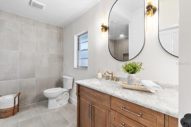 bathroom featuring toilet, vanity, tile patterned floors, and tile walls