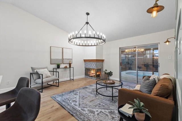 living room with lofted ceiling, a tiled fireplace, an inviting chandelier, and light wood-type flooring