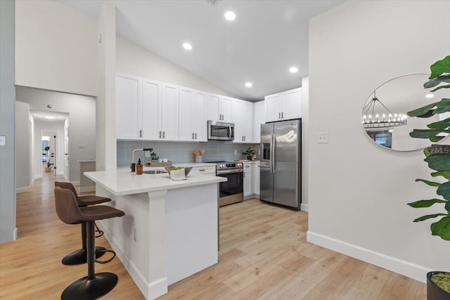 kitchen with stainless steel appliances, white cabinetry, lofted ceiling, a kitchen bar, and kitchen peninsula