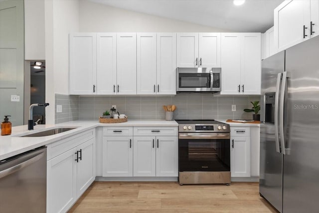 kitchen with stainless steel appliances, sink, white cabinetry, lofted ceiling, and tasteful backsplash