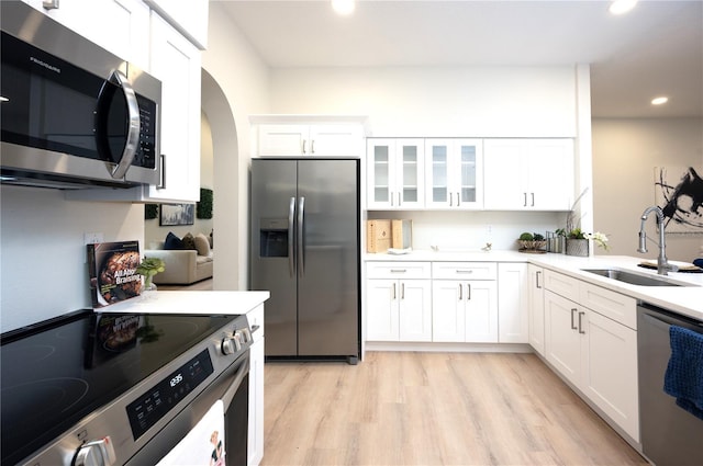 kitchen with appliances with stainless steel finishes, sink, white cabinetry, and light hardwood / wood-style flooring