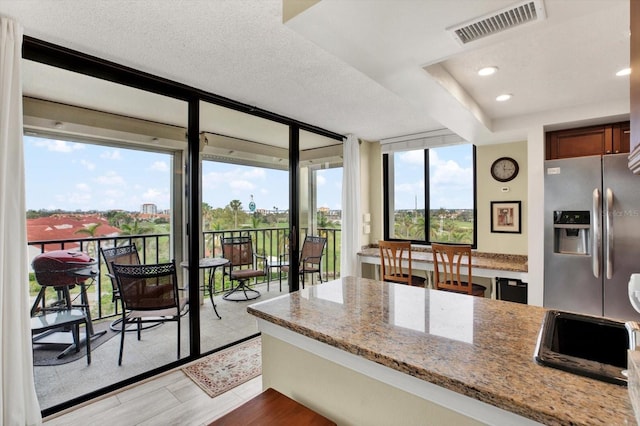 kitchen with light hardwood / wood-style floors, a textured ceiling, light stone counters, stainless steel refrigerator with ice dispenser, and floor to ceiling windows