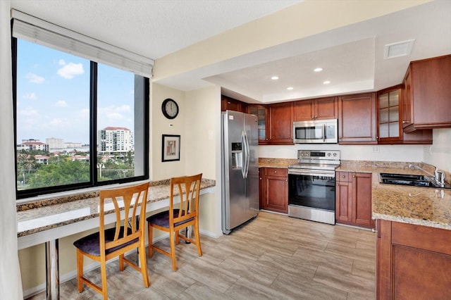 kitchen featuring stainless steel appliances, built in desk, sink, and light stone countertops