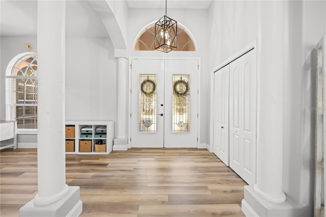 foyer featuring light hardwood / wood-style floors, a towering ceiling, french doors, a chandelier, and ornate columns