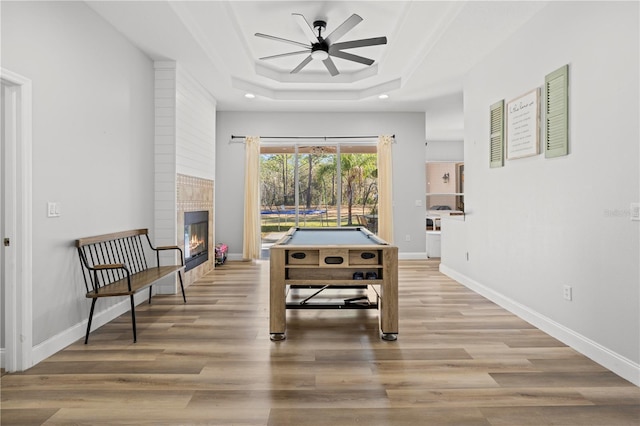 rec room with ceiling fan, a raised ceiling, a large fireplace, light hardwood / wood-style flooring, and pool table