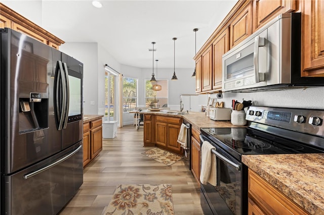 kitchen with pendant lighting, sink, light hardwood / wood-style flooring, light stone countertops, and appliances with stainless steel finishes