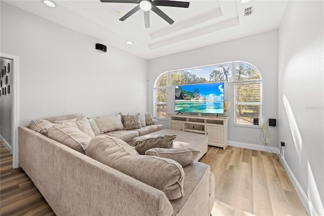 living room featuring a raised ceiling, light wood-type flooring, and ceiling fan