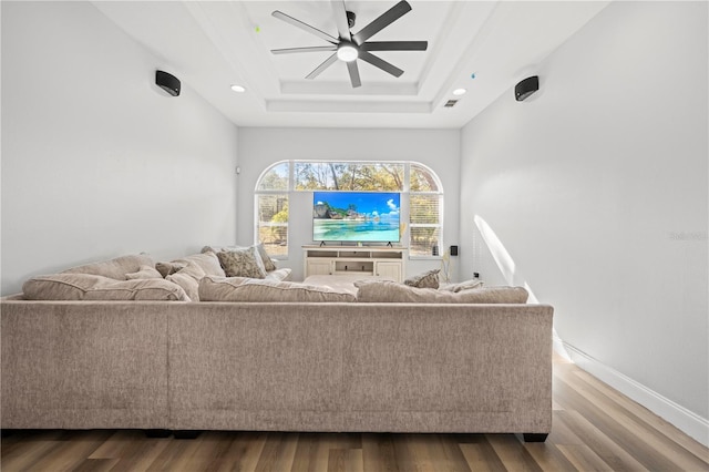 living room featuring ceiling fan, a raised ceiling, and wood-type flooring