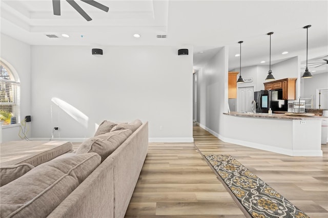 living room featuring ceiling fan, a raised ceiling, sink, and light hardwood / wood-style floors