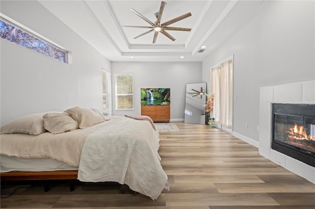 bedroom with ceiling fan, hardwood / wood-style flooring, a tile fireplace, and a tray ceiling