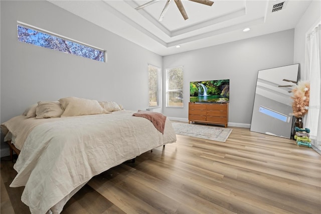 bedroom featuring ceiling fan, a tray ceiling, and light hardwood / wood-style flooring